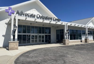 A three-quarter (angled) exterior view of the center. The white, barn-inspired building has a steep gabled roof, stone column bases, and a pergola-style canopy over the glass entrance.